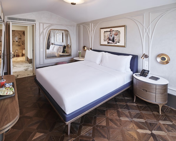 A hotel room with a large bed, a bedside table with a phone, a mirror, and a painting on the wall.