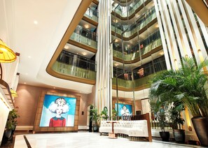 A modern hotel lobby with a high ceiling, multiple floors, a central staircase, and a large digital clock mural. - Les Temps Istanbul Karakoy, Curio Collection By Hilton (Istanbul)
