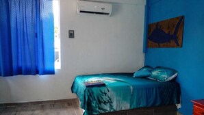 Una camera da letto con un letto, una parete blu, un condizionatore d'aria e una finestra con tende azzurre.