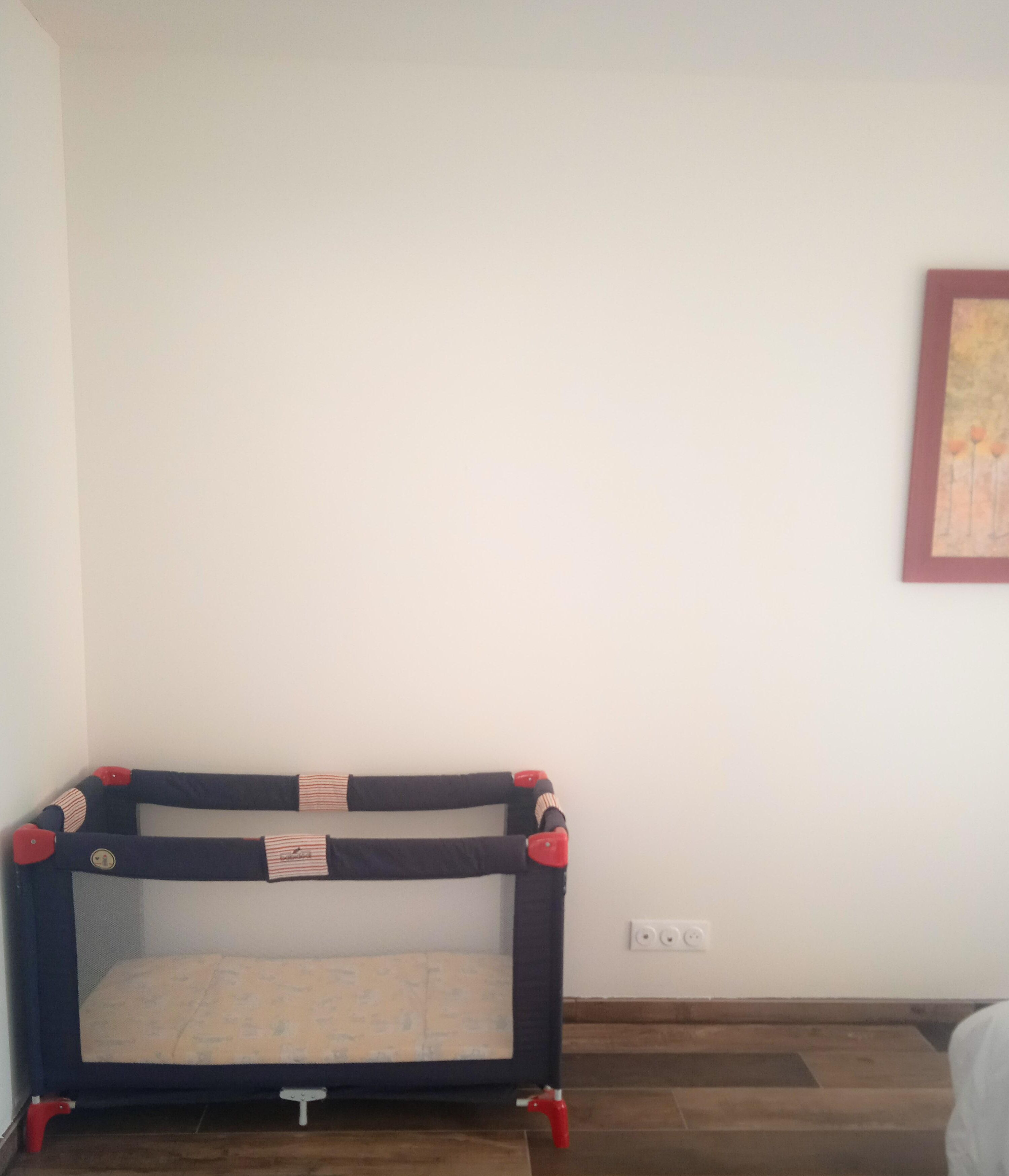 Una cama individual con colchón y cabecera, un enchufe en la pared y un cuadro enmarcado.