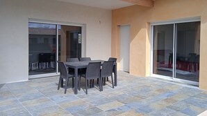 A patio with a table and chairs, a sliding glass door, and a tiled floor.