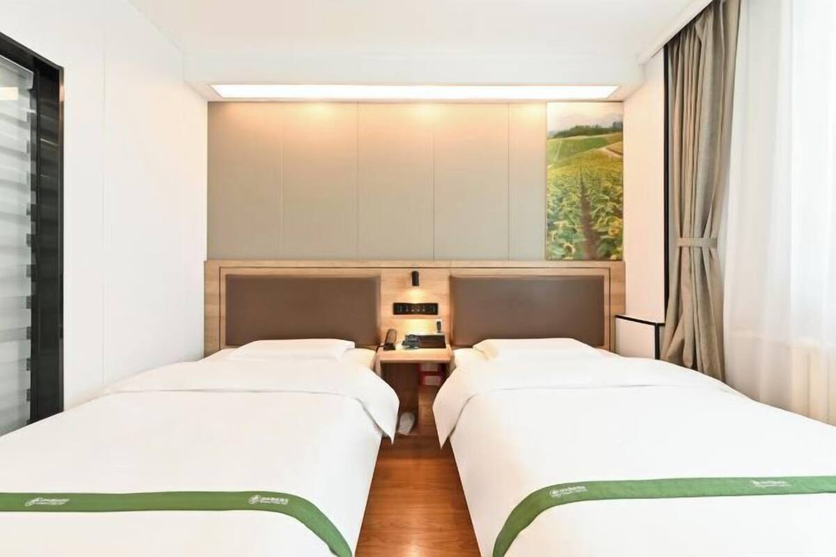 A hotel room with two beds, a desk, a nightstand, a wall-mounted TV, and a window with curtains.