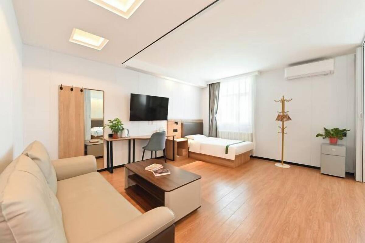 A modern hotel room with a sofa, a desk, a bed, a TV, and a coat stand.