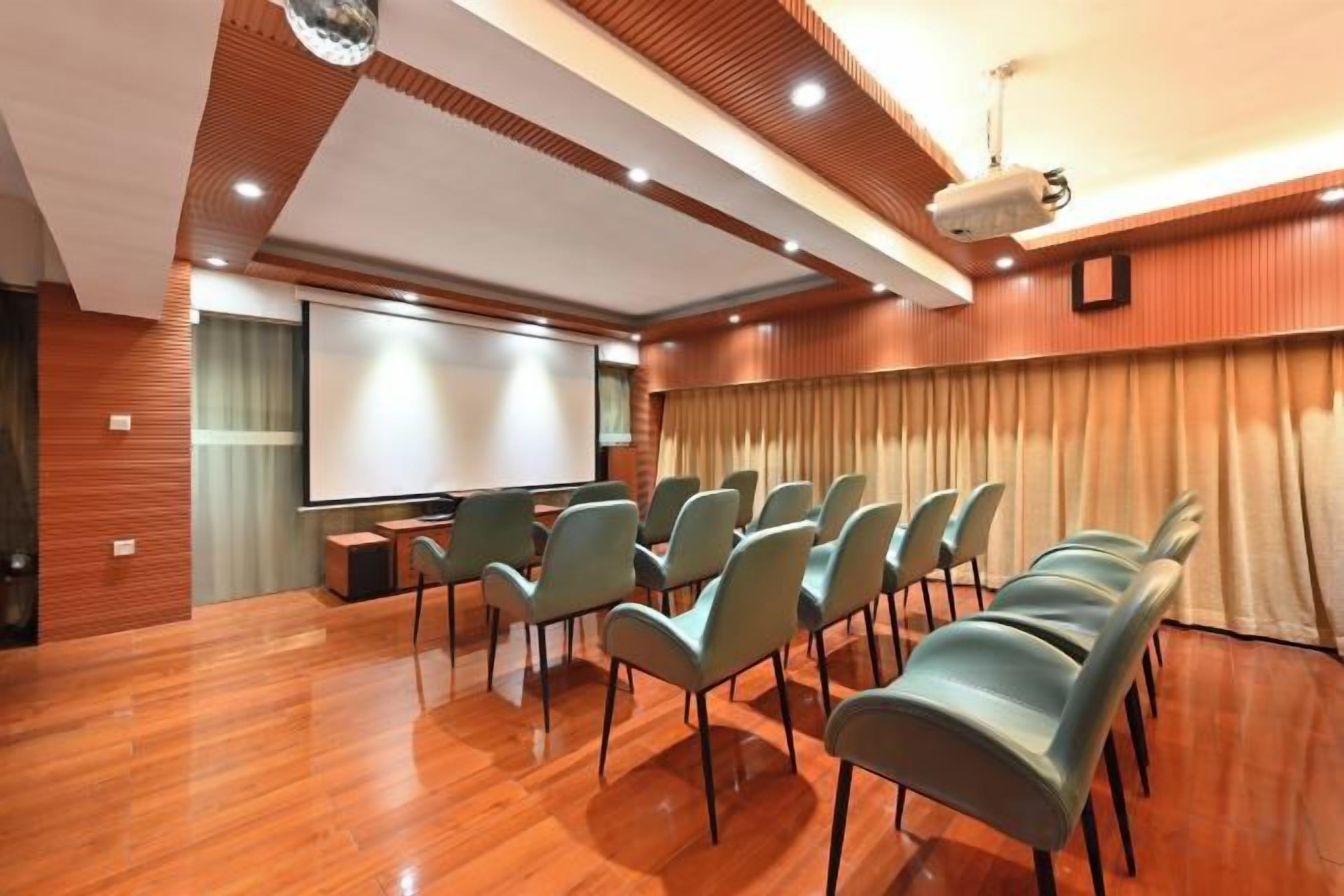 A conference room with a projector screen, rows of chairs, and a wooden floor.