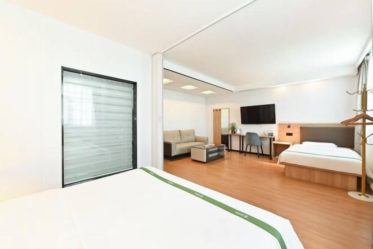 A modern hotel room with a bed, a desk, a sofa, and a television.