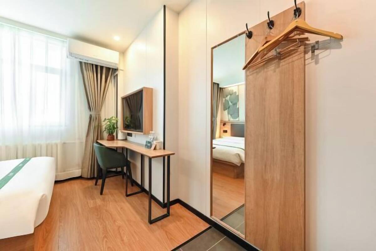 A hotel room with a bed, desk, chair, mirror, and a wardrobe.