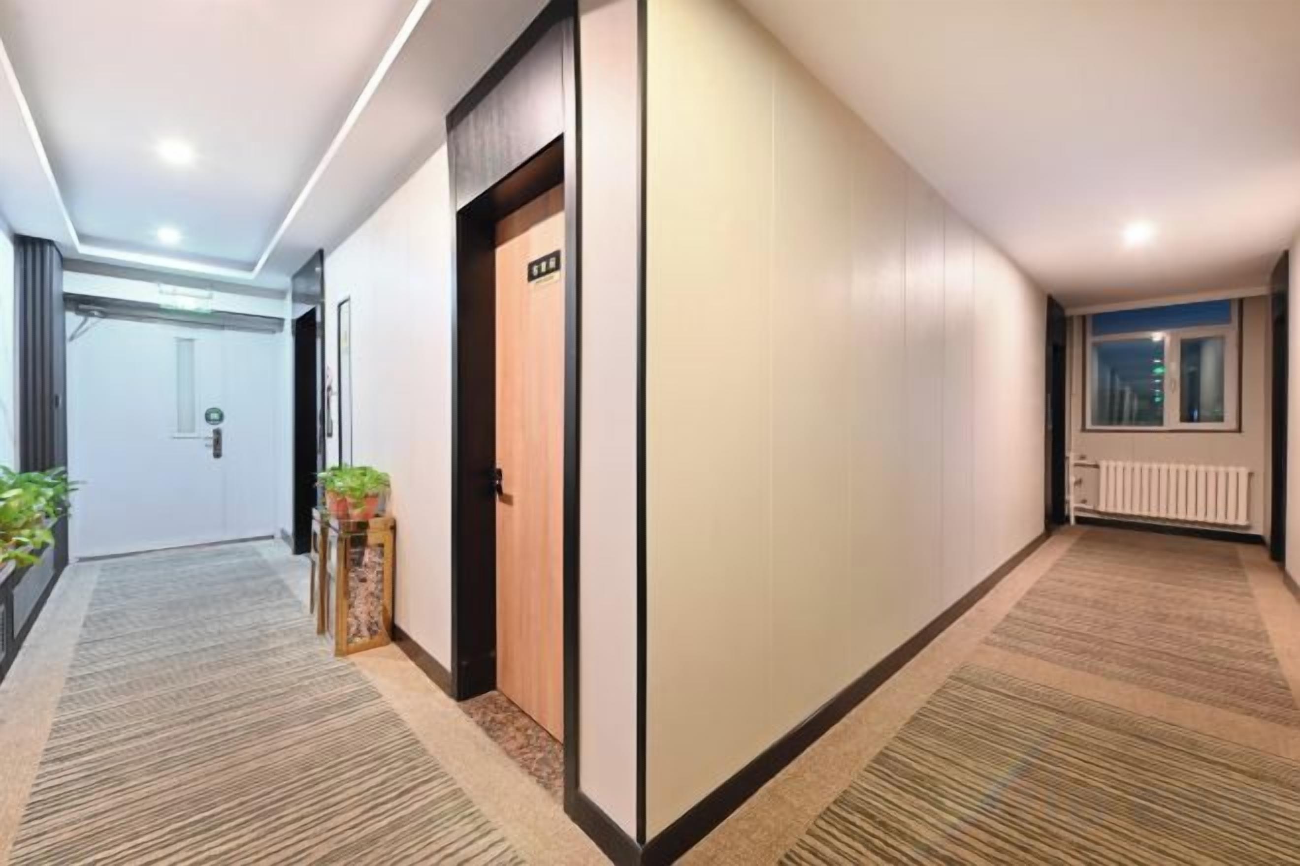 Un couloir d’hôtel avec un sol recouvert de moquette, une porte avec une pancarte et un radiateur fixé au mur.