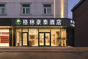 Een hotelingang met een bord in Chinese karakters, een glazen deur en een zichtbaar interieur met planken en planten.