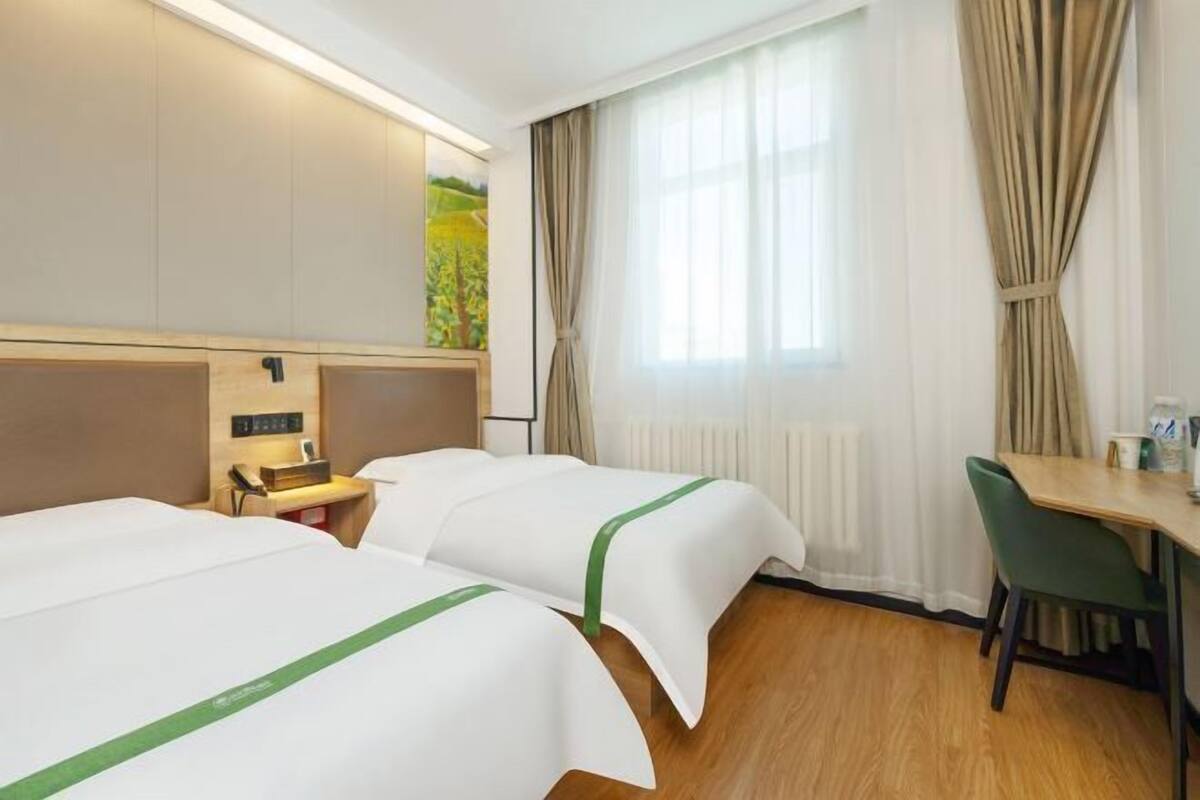 A hotel room with two beds, a desk, a chair, and a window with curtains.