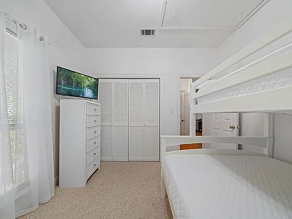 A bedroom with a bunk bed, a TV on a dresser, and a closet with sliding doors. - Beachwood Bliss (Destin)