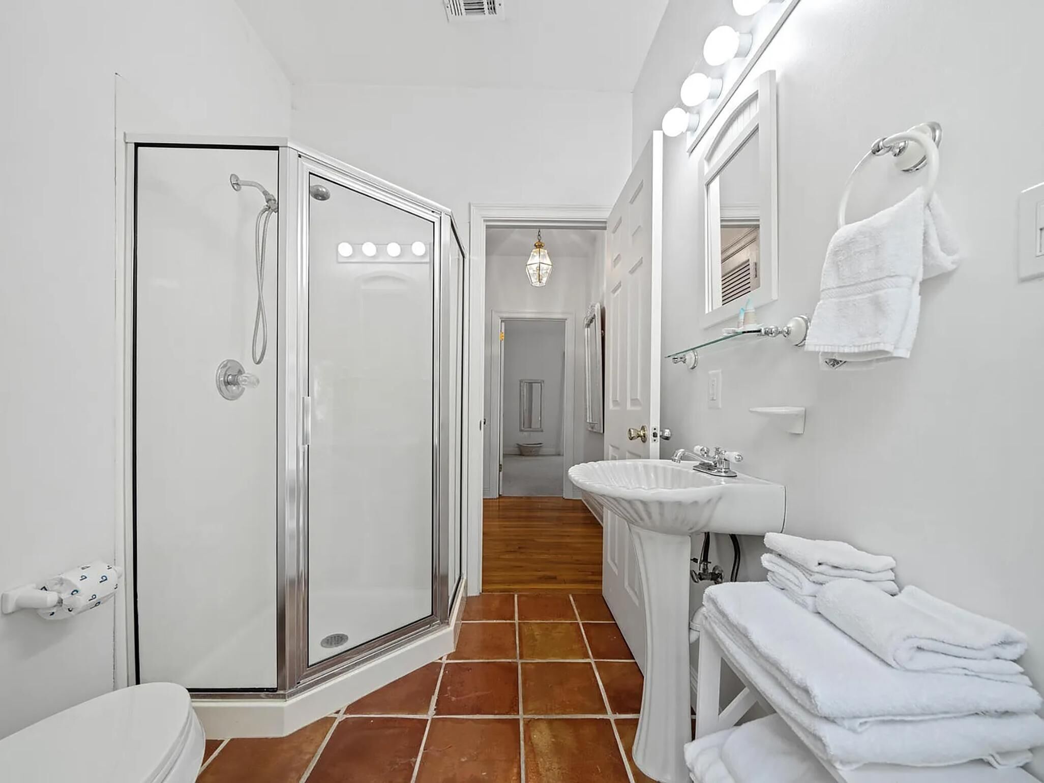 A bathroom with a glass-enclosed shower, a white sink, and a mirror with lights.