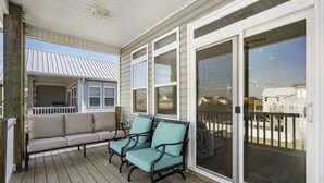 Une véranda abritée avec un canapé et des fauteuils, de grandes portes-fenêtres coulissantes et une vue sur les maisons voisines.