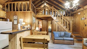 Ein Holzblockhaus-Innenraum mit Küche, Essbereich und einer Treppe zu einem Schlafboden.