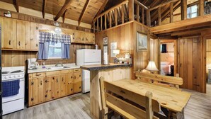 Ein rustikales Blockhaus-Interieur mit Holzwänden, einer Küche mit Herd, Kühlschrank und einem Essbereich mit einer Bank.