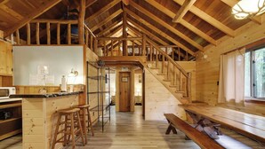 A cabin interior with a kitchen, dining area, and a staircase leading to a loft bedroom. - Cozy Lake Cabin #3 w/boatdock (Palmyra Township)