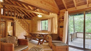 A wooden cabin interior with a staircase, a dining table, and a large window overlooking a forest. - Cozy Lake Cabin #3 w/boatdock (Palmyra Township)