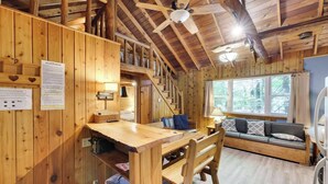 A wooden cabin interior with a dining area, a sofa, and a staircase. - Cozy Lake Cabin #4 w/boatdock (Palmyra Township)