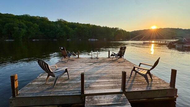 A wooden dock with two chairs facing a sunset over a lake, surrounded by trees. - Cozy Lake Cabin #4 w/boatdock (Palmyra Township)