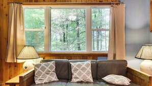 A cozy room with a leather sofa, two lamps, and a large window with curtains. - Cozy Lake Cabin #4 w/boatdock (Palmyra Township)