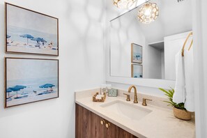 A bathroom with a large mirror, a sink, and two framed beach paintings. - Mimi's Pearl (Santa Rosa Beach)