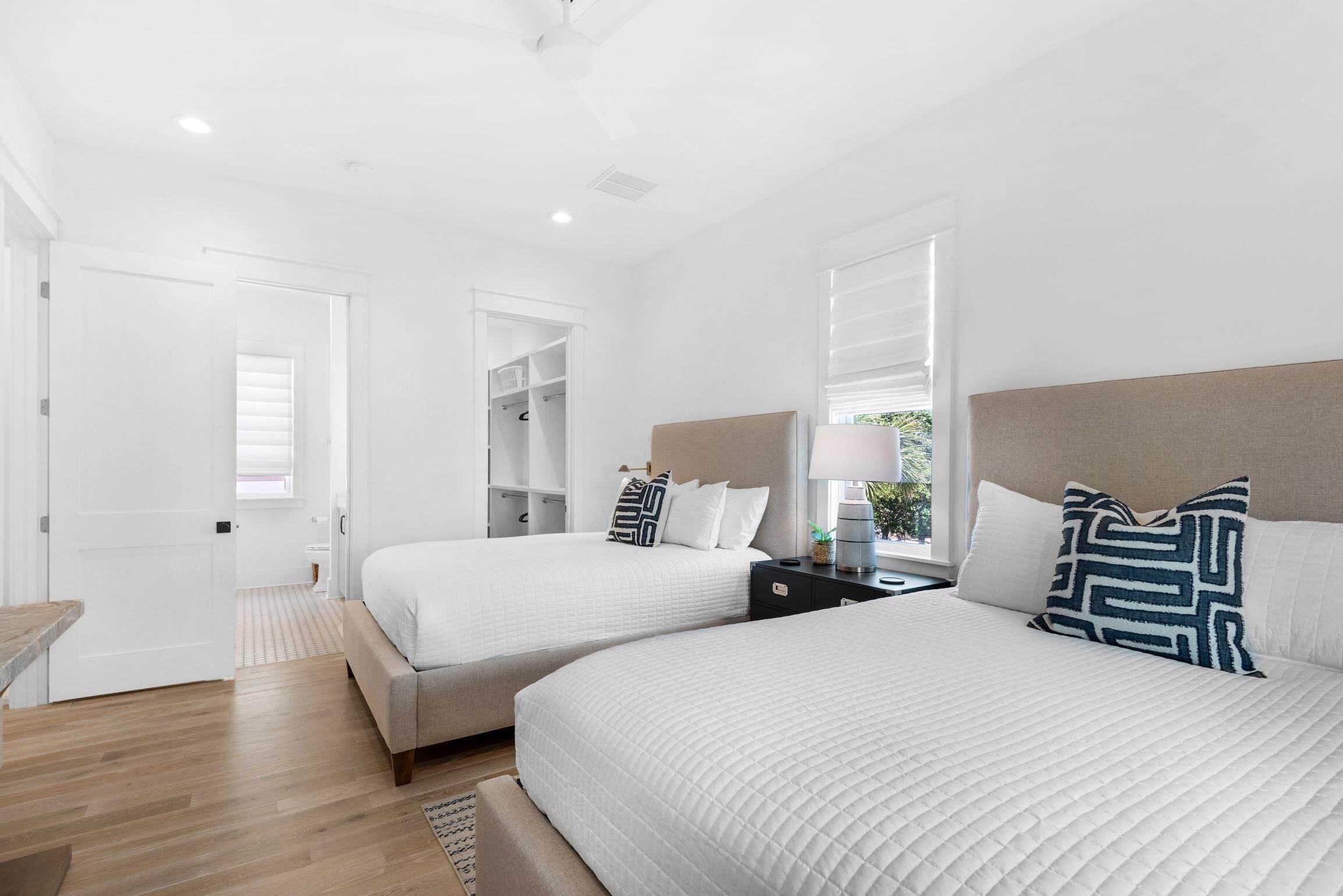 Une chambre d’hôtel moderne avec deux lits, un plancher en bois, un placard et une fenêtre avec des stores.