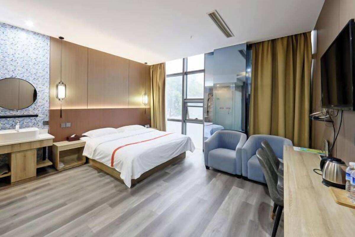 Une chambre d’hôtel comprenant un lit, un bureau avec une chaise, une télévision, une fenêtre avec des rideaux et une salle de bain avec un miroir et un lavabo.