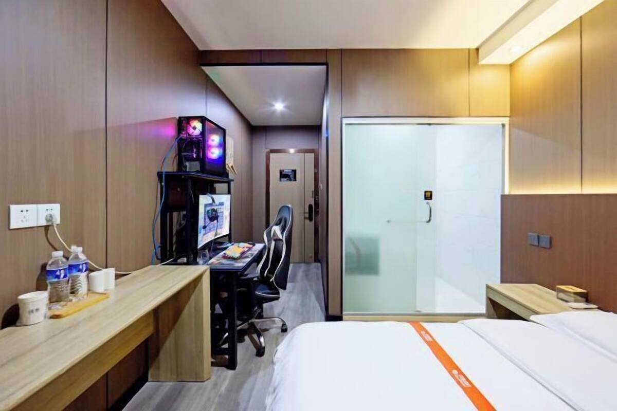 Une chambre d’hôtel équipée d’un bureau, d’un ordinateur, d’une chaise, d’un lit et d’une porte en verre donnant sur une salle de bain.
