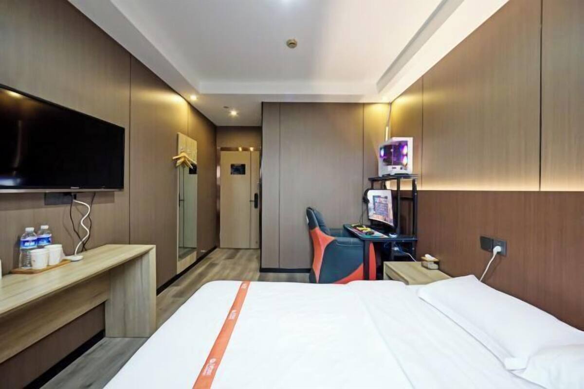 Une chambre d’hôtel avec un lit, un bureau avec un ordinateur, une télévision et un miroir.