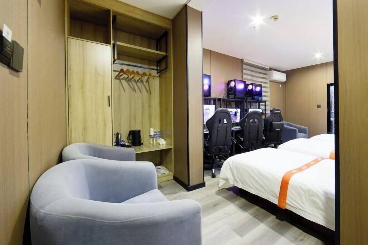 Une chambre d’hôtel comprenant un lit, deux fauteuils, un bureau avec un ordinateur et une armoire.