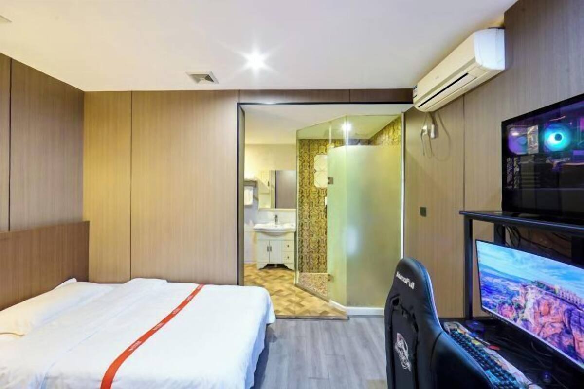 Une chambre d’hôtel équipée d’un lit, d’un bureau avec un ordinateur, d’un climatiseur et d’un espace douche.