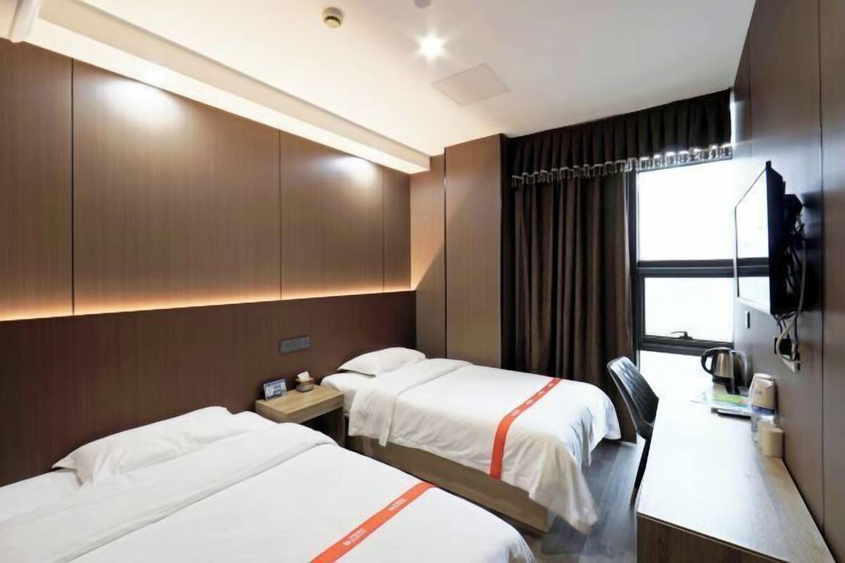 Une chambre d’hôtel avec deux lits, un bureau, une chaise, une télévision et une fenêtre avec des rideaux.