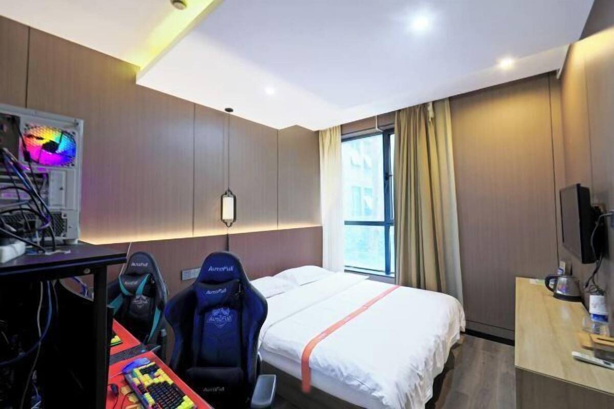 Une chambre d’hôtel équipée d’un lit, d’un bureau avec un ordinateur et un clavier, d’un fauteuil de jeu et d’une télévision.
