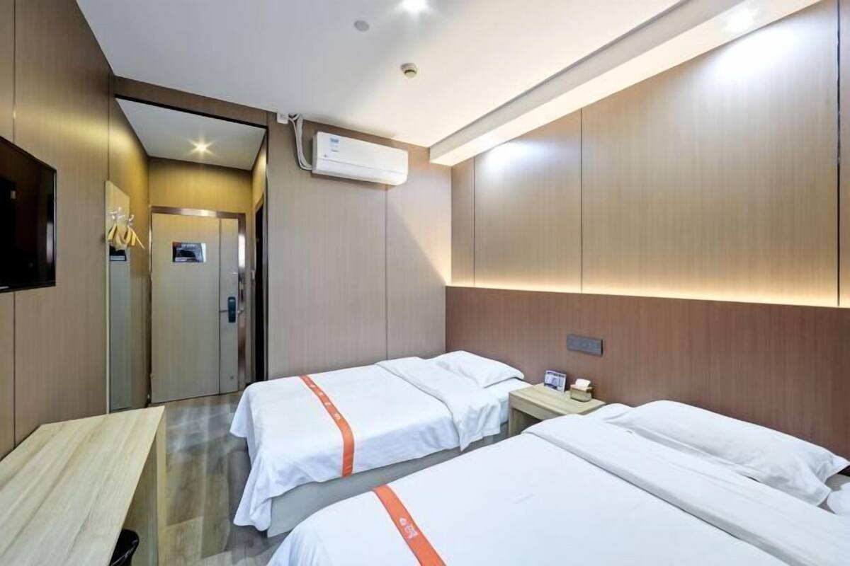 Une chambre d’hôtel avec deux lits, une tête de lit en bois, un appareil de climatisation et un téléviseur fixé au mur.