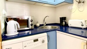 Una cocina compacta equipada con microondas, hervidor, cafetera y lavadora.