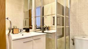Ein modernes Badezimmer mit einer Duschkabine aus Glas, einem weißen Waschbecken mit einer hölzernen Seifenschale und einer Toilette.
