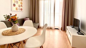 Ein modernes Wohnzimmer mit einem runden Esstisch, weißen Stühlen, einer Couch und einem TV-Schrank.