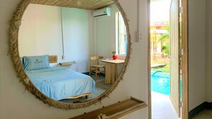 Een slaapkamer met een bed, een stoel, een kleine tafel en een grote spiegel aan de muur.