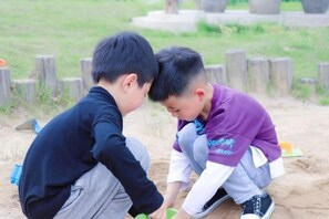 Dos niños jugando en una zona arenosa, con postes de madera al fondo.