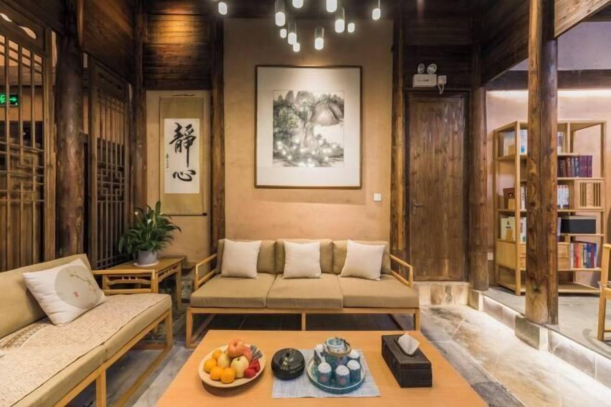A cozy room with a sofa, a small table with fruit and a teapot, and a framed artwork on the wall.