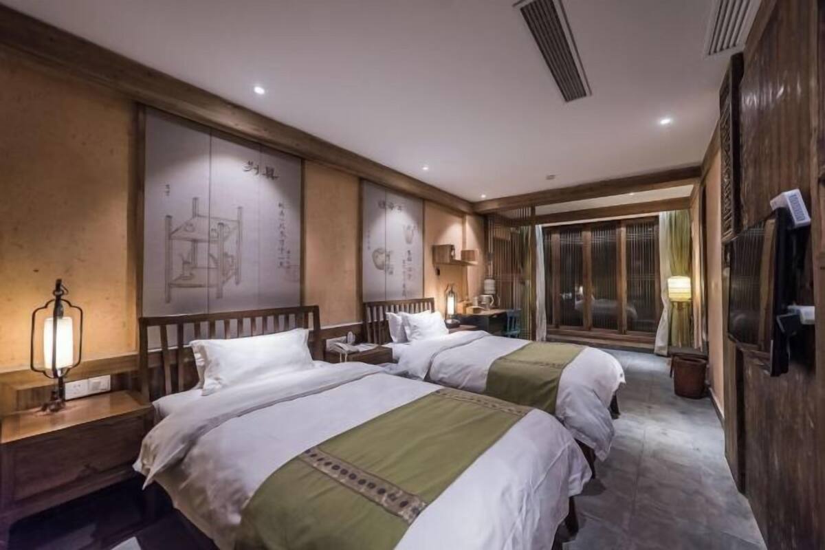 A hotel room with two beds, a desk, a chair, a lamp, and a sliding door leading to a balcony.