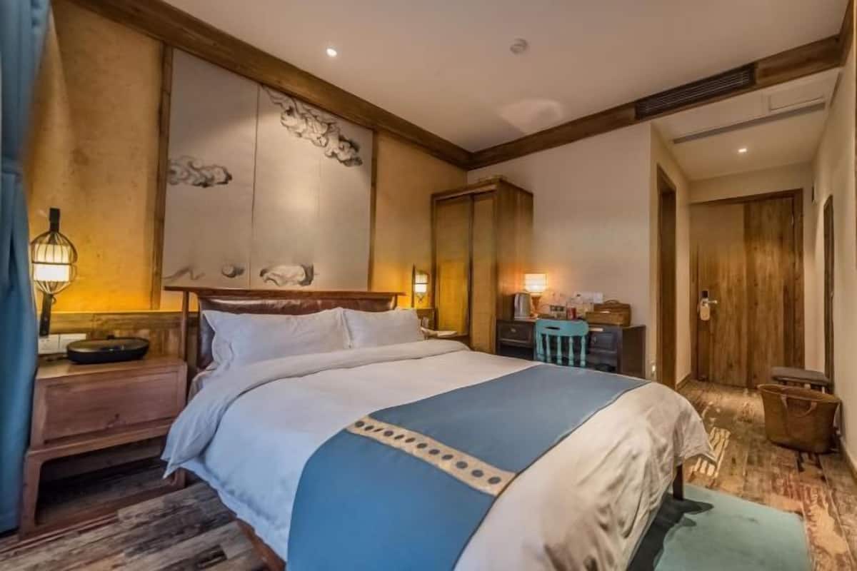 A hotel room with a large bed, a wooden headboard, a nightstand, a desk, and a wardrobe.