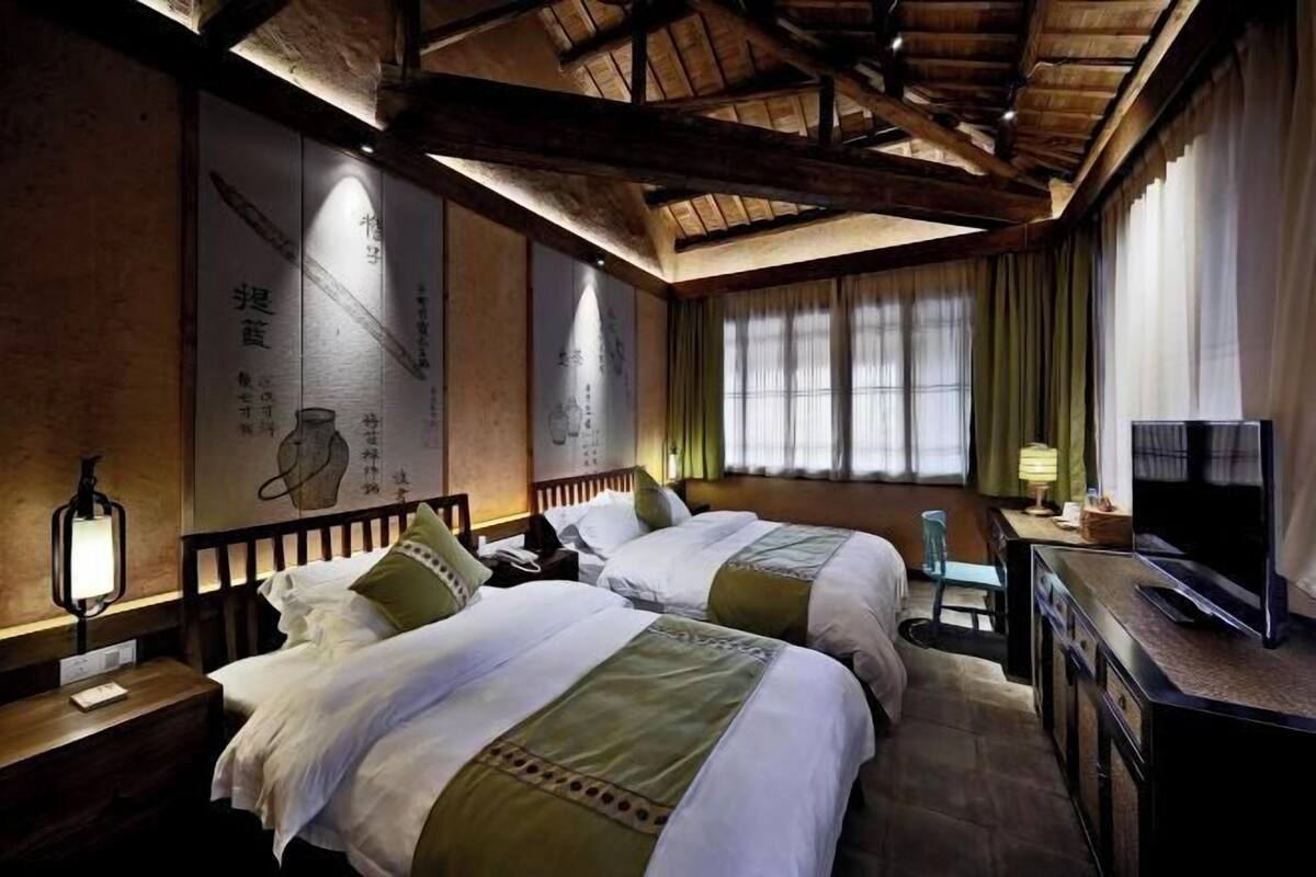 A hotel room with two beds, a television, a desk, and a window with curtains.