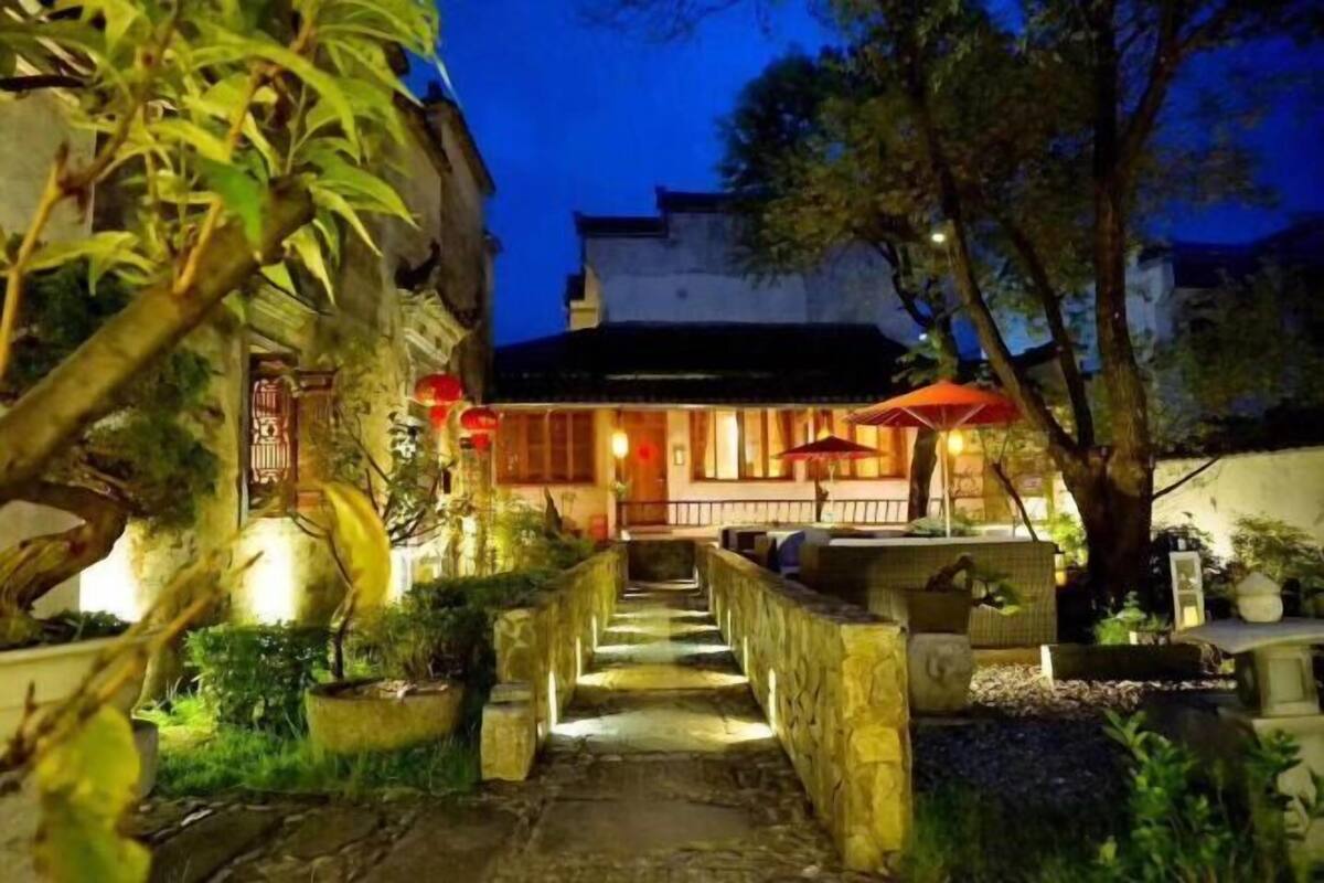 A stone pathway leading to a building with traditional architecture, surrounded by greenery and illuminated by warm lighting.