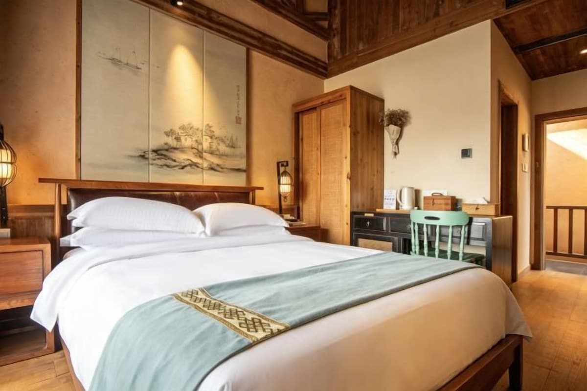 Une chambre d’hôtel avec un grand lit, un bureau avec une chaise, une armoire en bois et un tableau au mur.