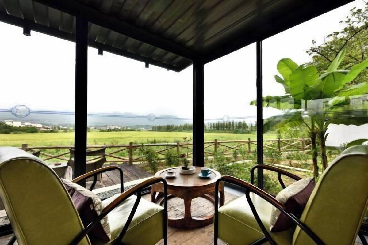 A covered outdoor seating area with chairs and a table, overlooking a green landscape and a body of water.