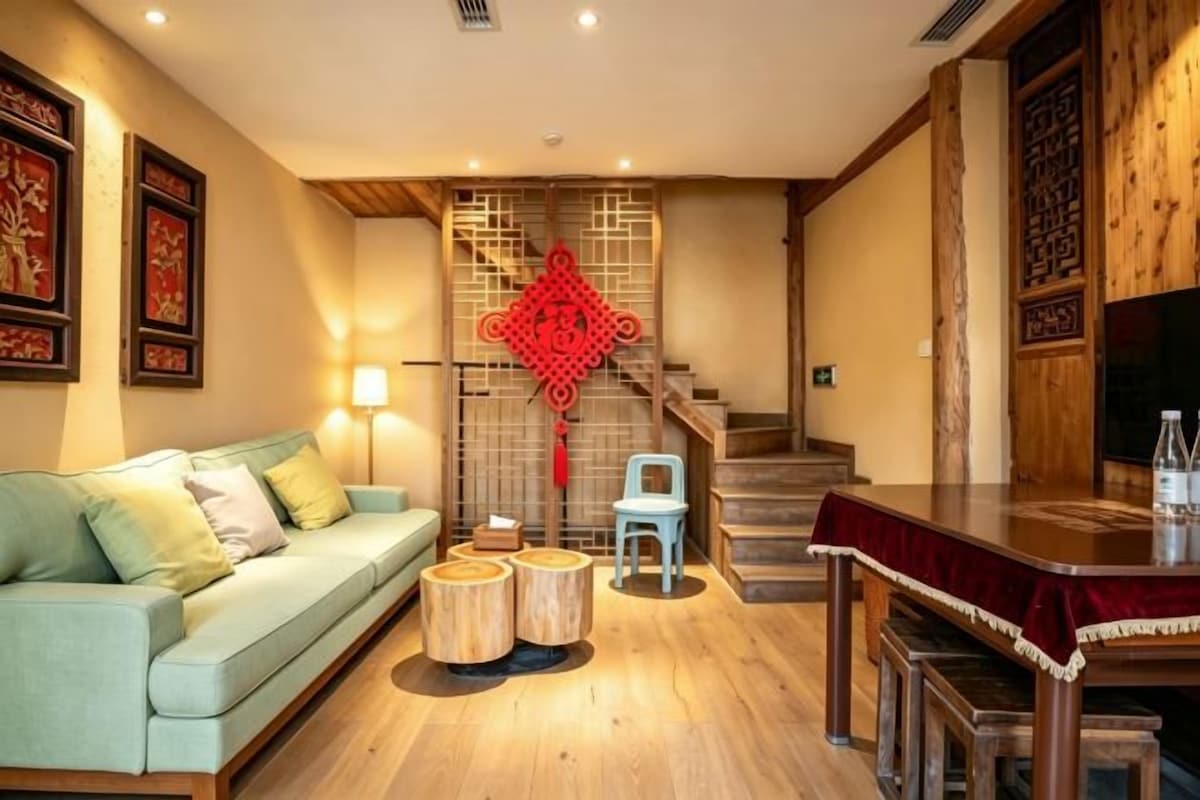 Un salon avec un canapé, des tables rondes en bois, une décoration murale rouge et un escalier.