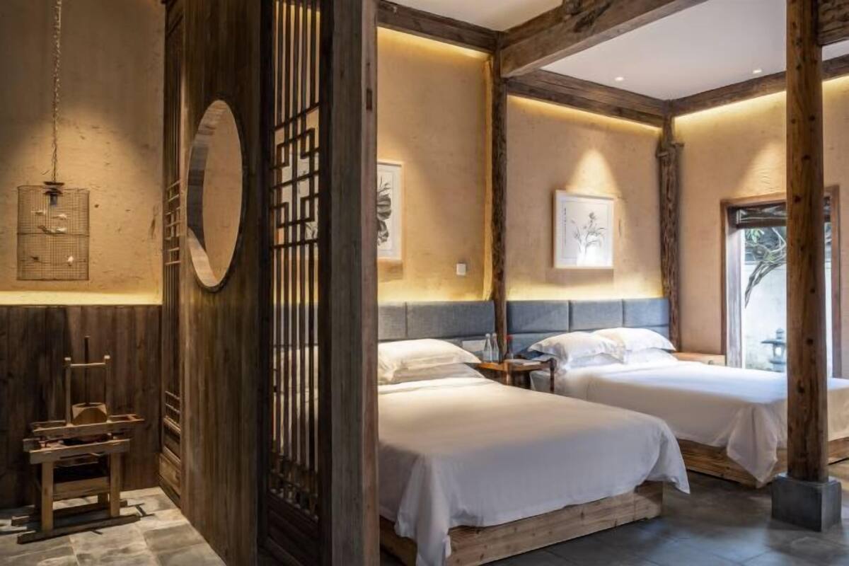 A room with two beds, wooden beams, and a decorative screen.