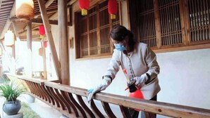 A person cleaning a wooden railing with a red spray bottle.
