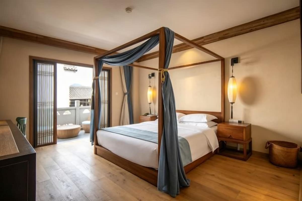 Un lit à baldaquin, une table de chevet avec une lampe et une vue sur l’extérieur grâce à une porte coulissante.