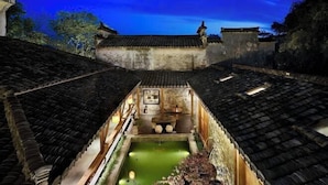A traditional courtyard with a central pond, surrounded by buildings with tiled roofs and wooden railings.